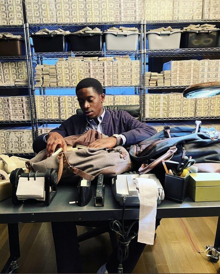 Franklin at a table stacked with ledgers and adding machines, shelves of banded cash behind him.