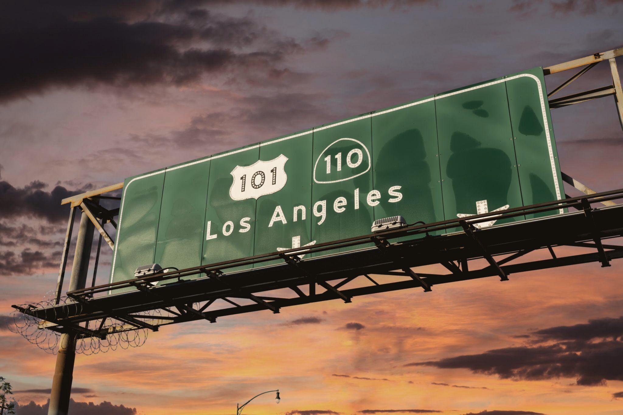 An overhead freeway sign for the 101 and 110 to Los Angeles, against a burning sunset sky.